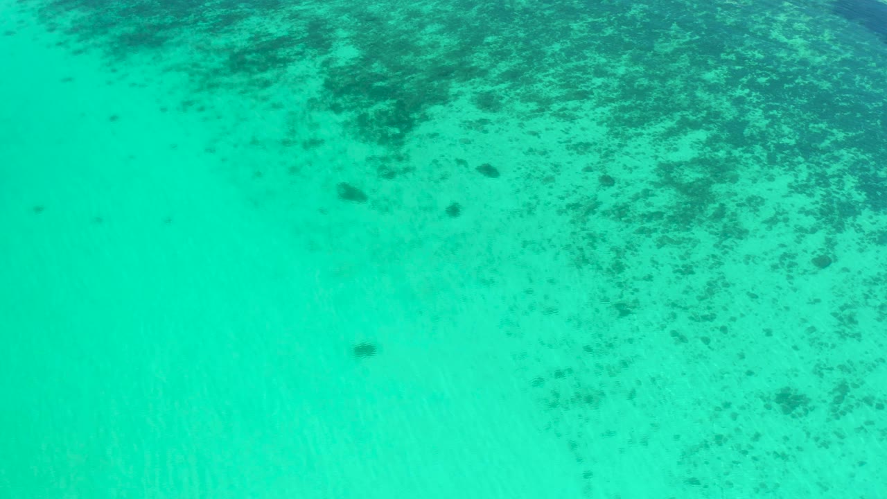 Turquoise shallow ocean in El Sargento La Ventana, Mexico, shows darker reef-like seabed patches near the top edge and open lighter water below, with no visible people.