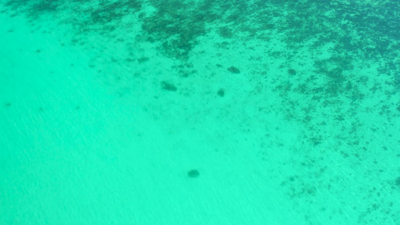 Overhead view of teal ocean water in El Sargento La Ventana, Mexico, with dark underwater patches concentrated near the upper frame and no visible people.