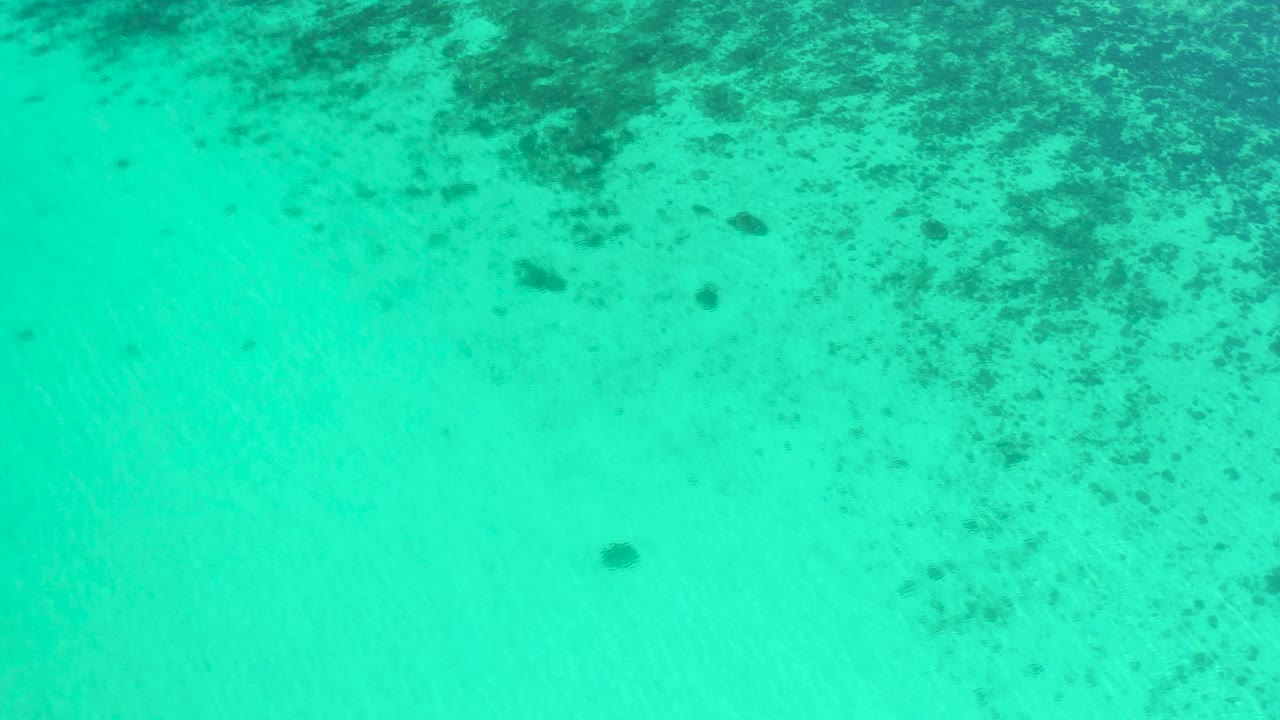 High overhead frame of teal water in El Sargento La Ventana, Mexico, with scattered darker seafloor texture across the top and center and no visible people.