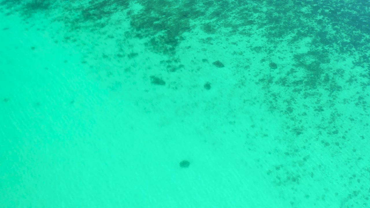 Clear turquoise ocean water in El Sargento La Ventana, Mexico, viewed from above with darker reef or seaweed patches mostly along the upper portion and no visible people.