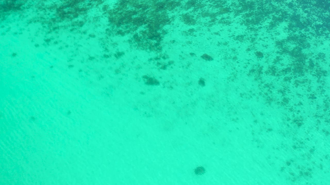 Top-down view of turquoise shallow water in El Sargento La Ventana, Mexico, with dark seabed patches near the top of frame and no visible people.