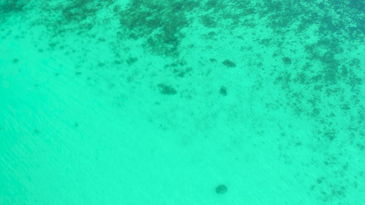 Aqua water over pale sand and seaweed patches.