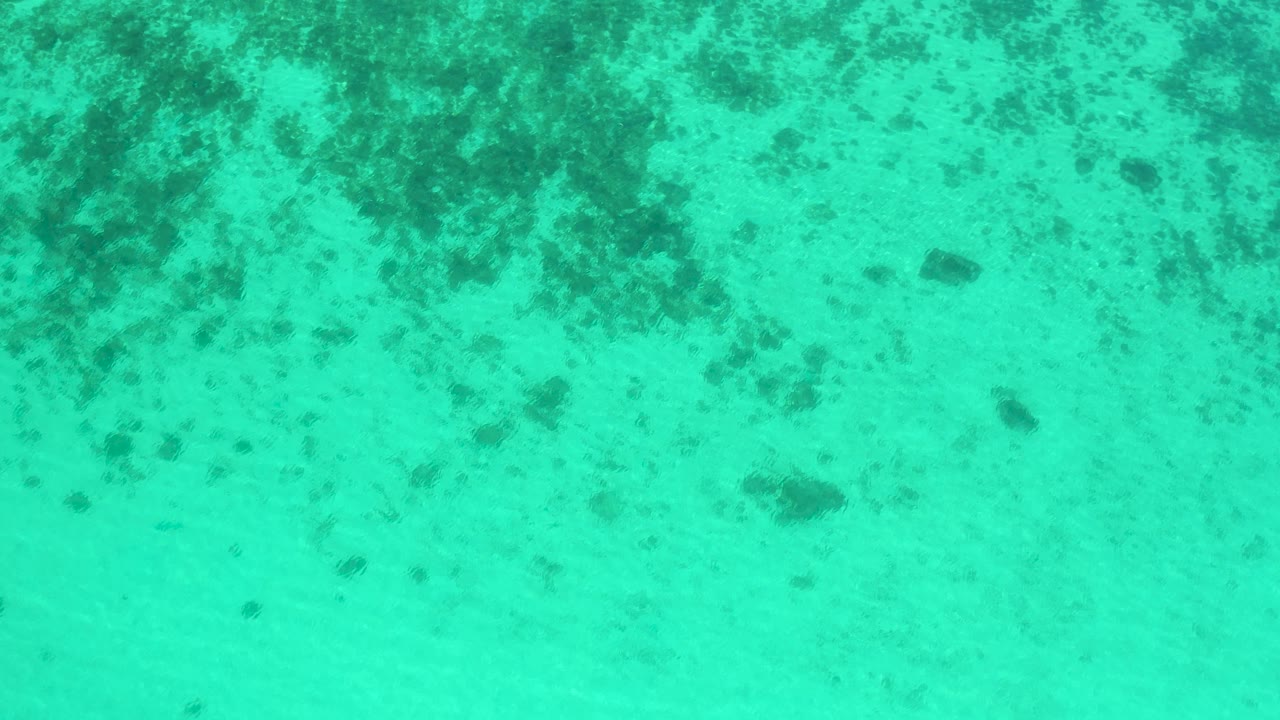 Aqua seawater fills the frame in El Sargento La Ventana, Mexico, with scattered darker underwater forms and no visible people.