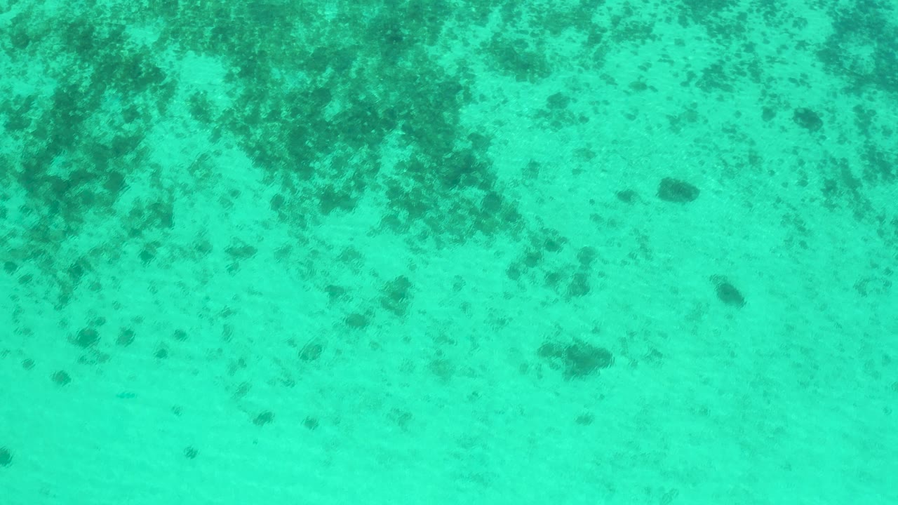 Downward view of shallow turquoise water in El Sargento La Ventana, Mexico, showing mottled seabed texture beneath a lightly rippled surface and no visible people.