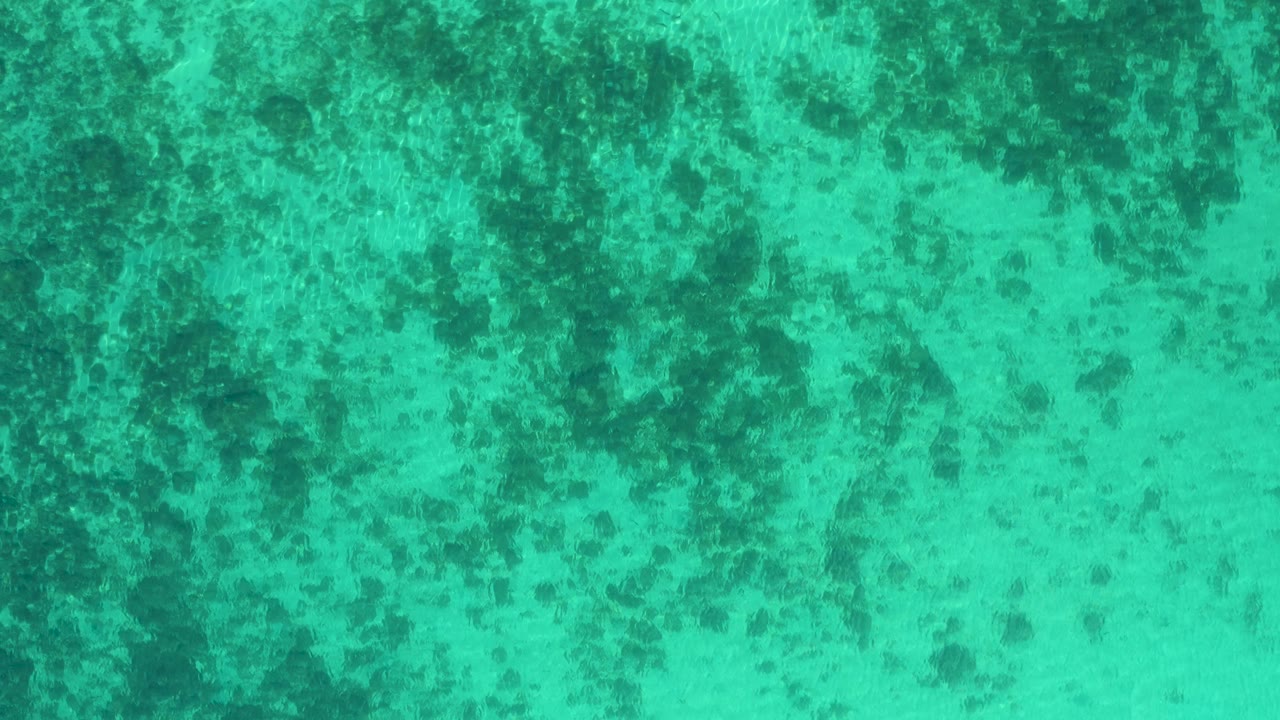 Third frame holds on clear turquoise ocean in El Sargento La Ventana, Mexico, where darker underwater patches form a loose diagonal pattern and no visible people appear.