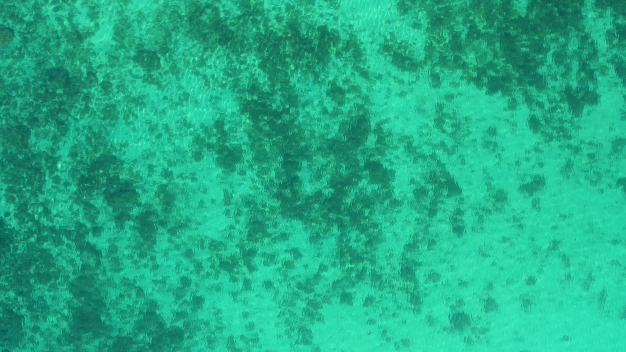 Top-down blue-green water with scattered submerged reef texture.