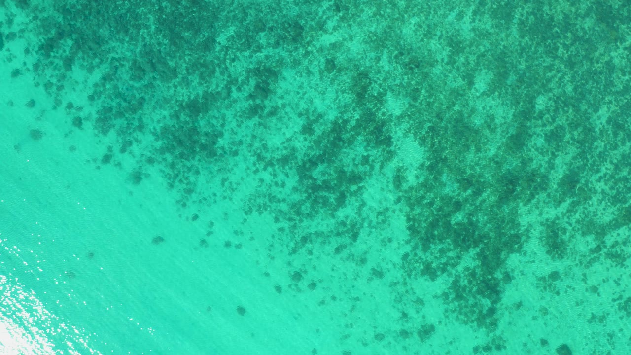 Aerial water view over El Sargento La Ventana, Mexico, with mottled dark bottom texture spreading across the upper frame and no visible people.