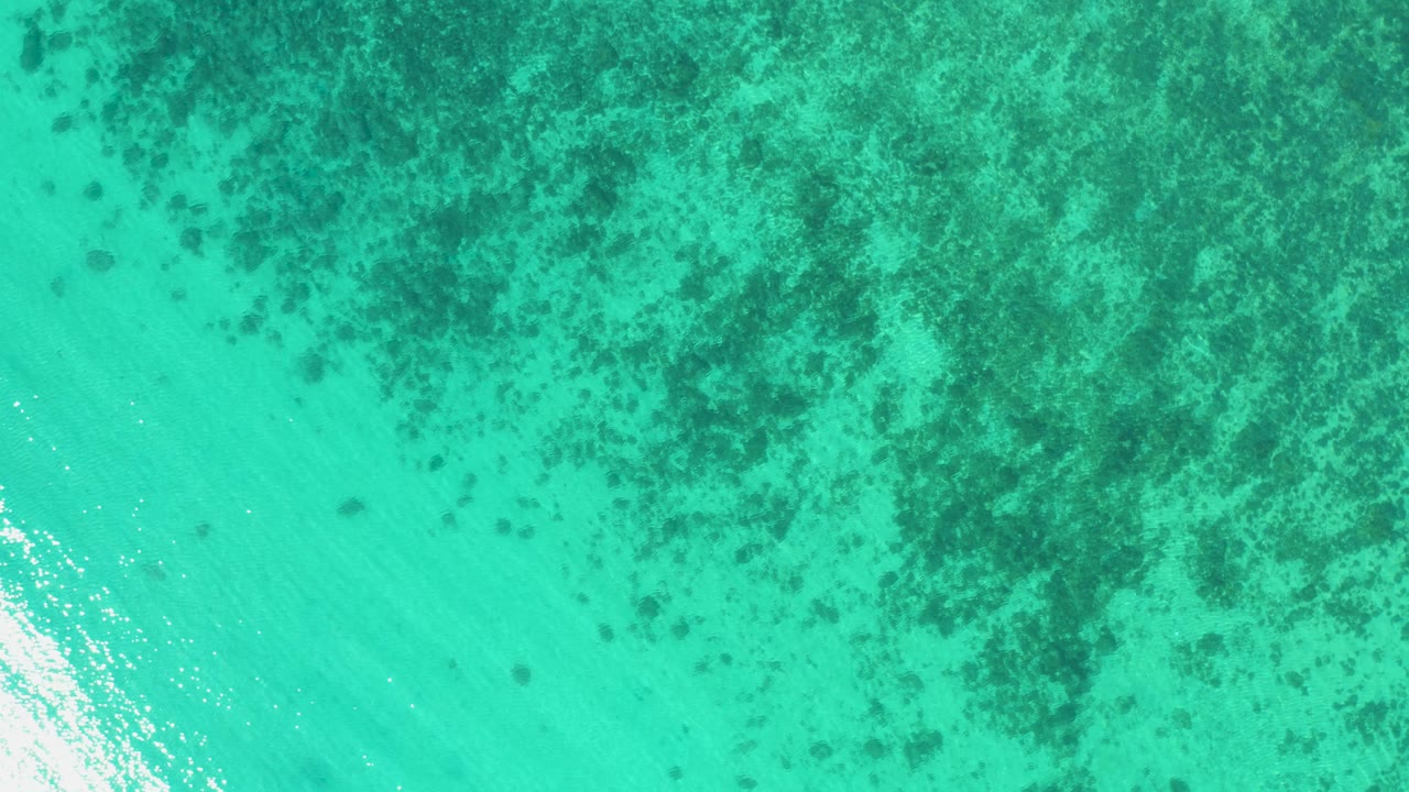 Overhead aerial frame in El Sargento La Ventana, Mexico, showing turquoise water, bright reflected sunlight near the lower right, and no visible people.