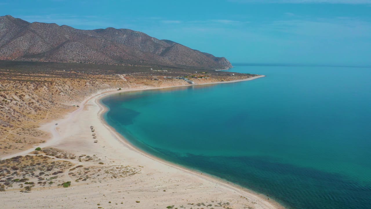 Drone view over desert beach and blue bay near mountains.
