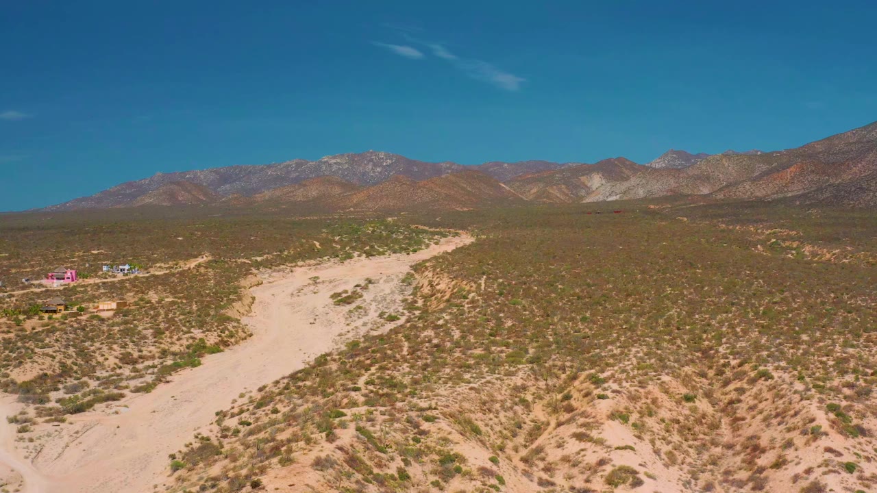 Aerial frame from El Sargento La Ventana, Mexico showing a pale sandy trail through cactus-dotted desert scrub with distant mountains and no visible people.