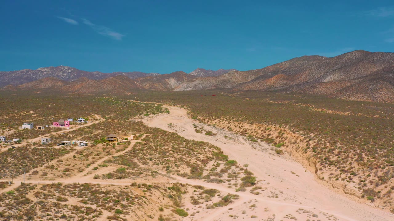 Aerial desert view with buildings, roads, wash, and ridges.