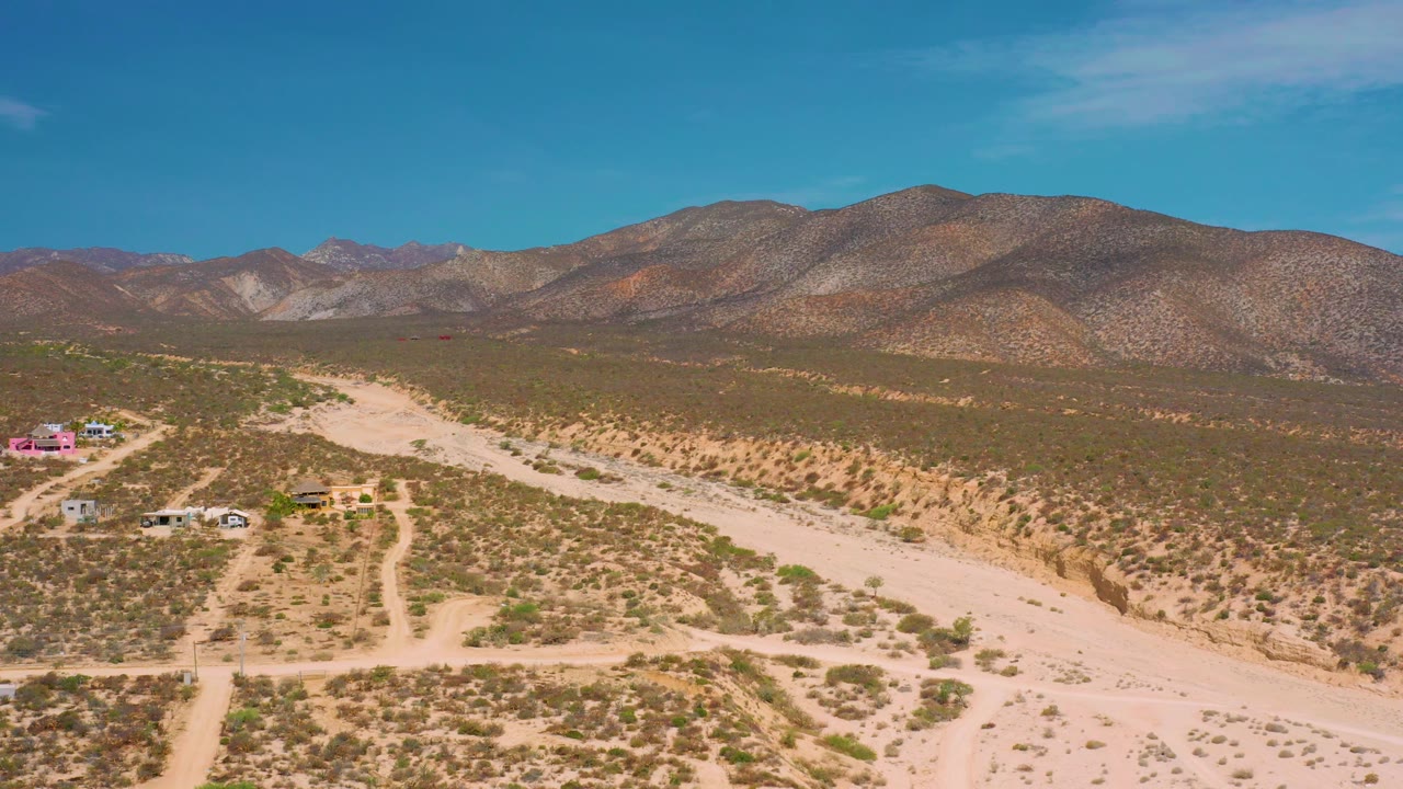 Desert aerial with mountains filling the background and a few buildings at frame edge