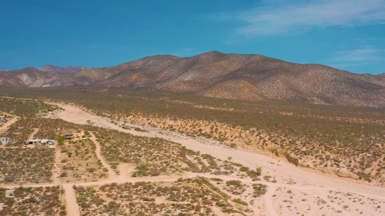 Early frame over El Sargento La Ventana, Mexico with branching dirt roads, a broad sandy channel, scrub-covered flats, distant rocky hills, and no visible people.