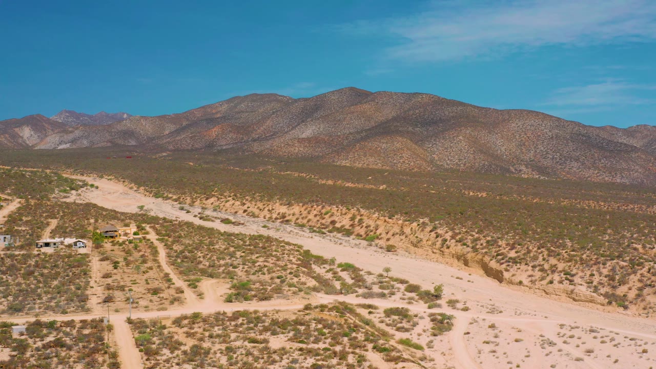 Wide frame from El Sargento La Ventana, Mexico looking across a dry wash and scrubland toward brown mountain ridges, with no visible people.