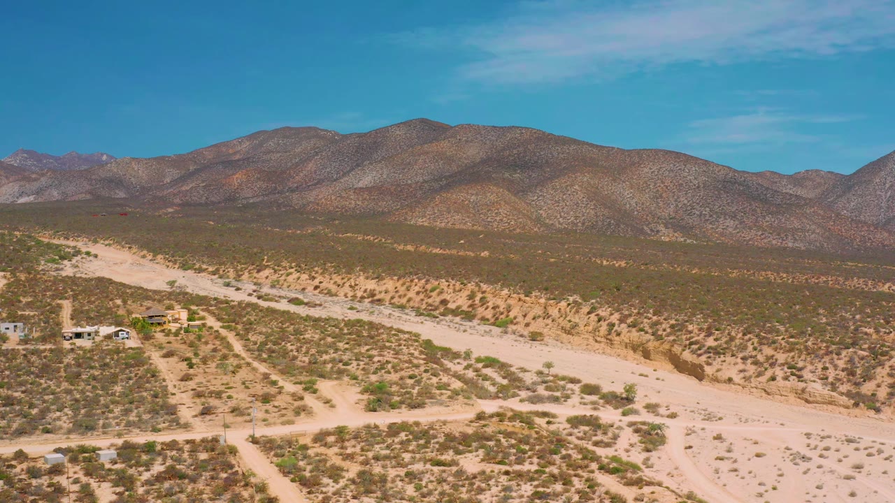 Wide aerial view of desert tracks and low mountains under blue sky.