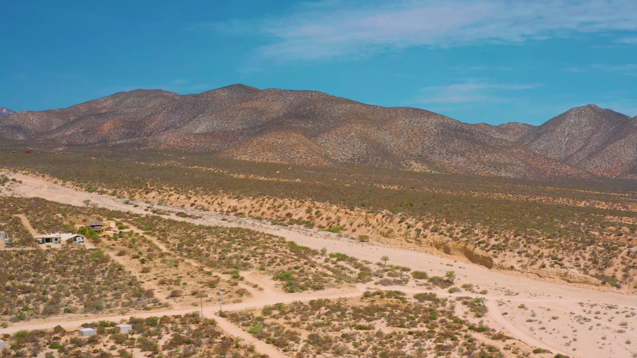 Early frame showing the dirt track running diagonally through El Sargento La Ventana scrubland, with brown mountains beyond and no visible people.