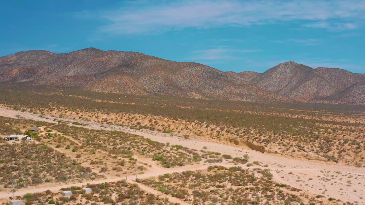 Arid scrubland crossed by pale dirt roads below a mountain ridge.