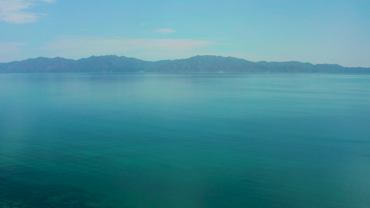 Opening frame of El Sargento La Ventana, Mexico, showing broad turquoise water, low mountains on the horizon, pale blue sky, and no visible people.