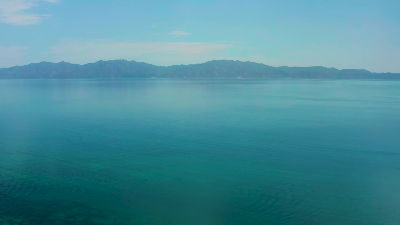 Second frame over El Sargento La Ventana water, with a darker blue foreground, thin ripples on the sea, distant mountains, clear sky, and no visible people.