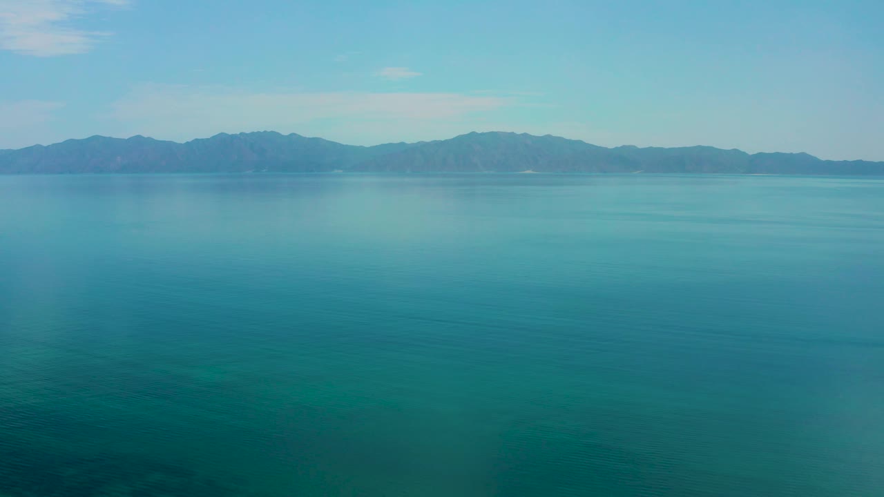 Third frame from El Sargento La Ventana with calm teal-blue sea, a continuous mountain ridge across the background, light sky, and no visible people.