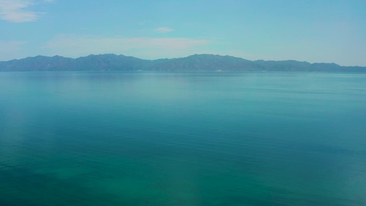 Blue-green water with distant mountain range and pale sky