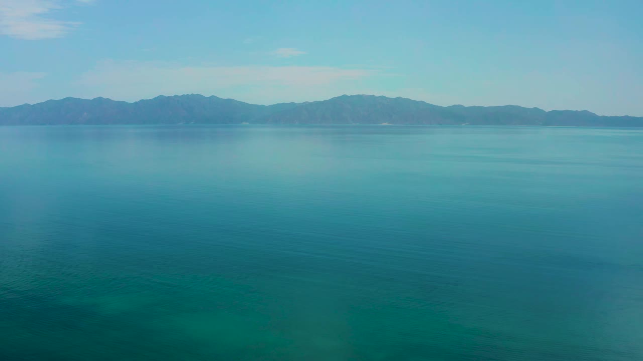 A second view of calm turquoise water in El Sargento La Ventana, Mexico, with the mountain ridge centered slightly higher in frame and no visible people.