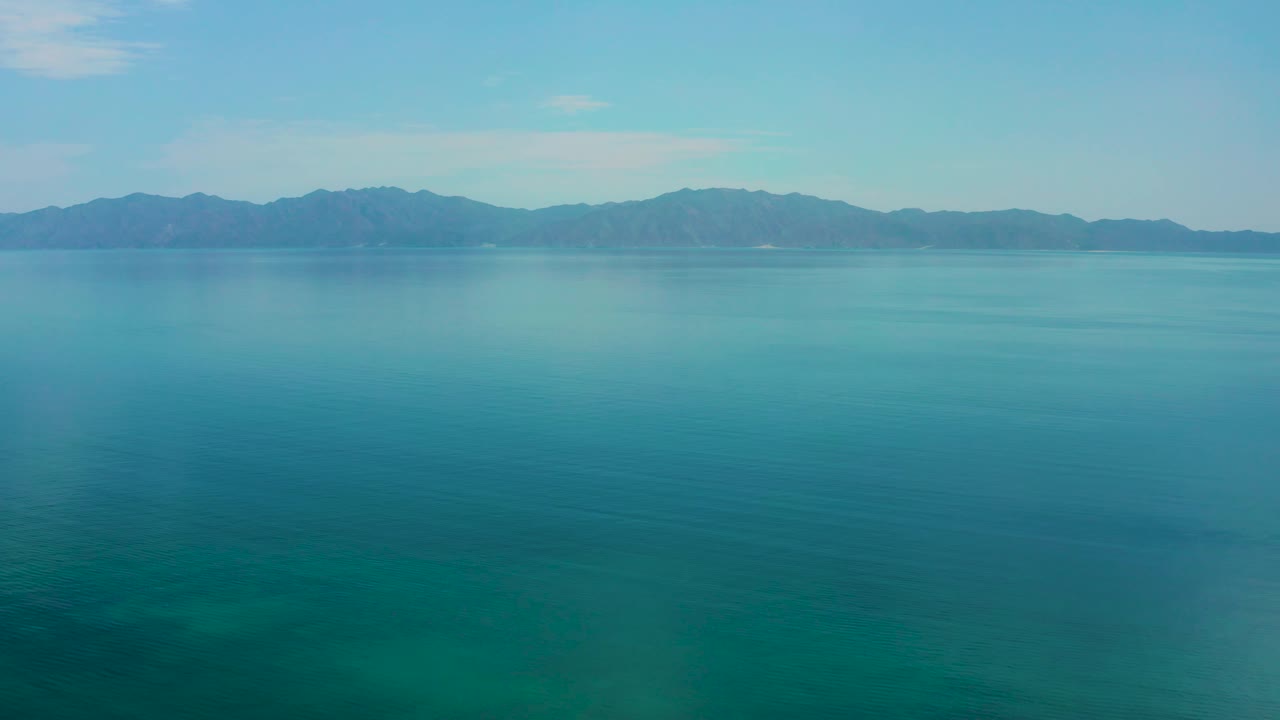 Wide blue water stretches toward distant mountains in El Sargento La Ventana, Mexico, with faint surface texture and no visible people.