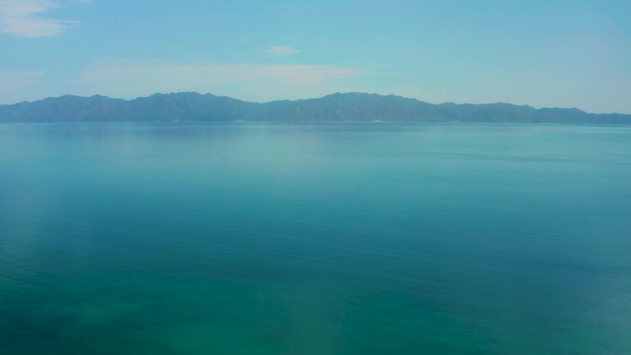 Open blue-green sea surface in El Sargento La Ventana, Mexico, sits below a dark mountain horizon and pale cloud patches, with no visible people.