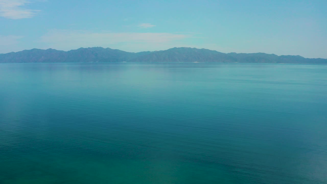 Wide view of blue-green water and a distant mountain range in El Sargento La Ventana, Mexico, with no visible people at the start of the clip.