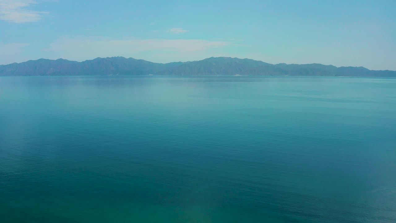Open blue water dominates the foreground while a hazy mountain range spans the background in El Sargento La Ventana, Mexico, with no visible people.