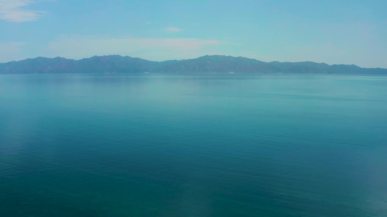 Second frame showing calm open water and darker mountain silhouettes across the horizon in El Sargento La Ventana, Mexico, with no visible people.