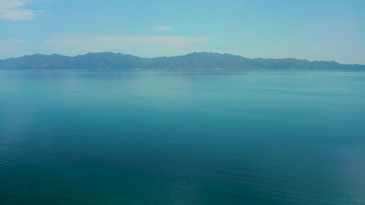 Mid-clip frame with a large expanse of blue water below a low mountain horizon in El Sargento La Ventana, Mexico, and no visible people.