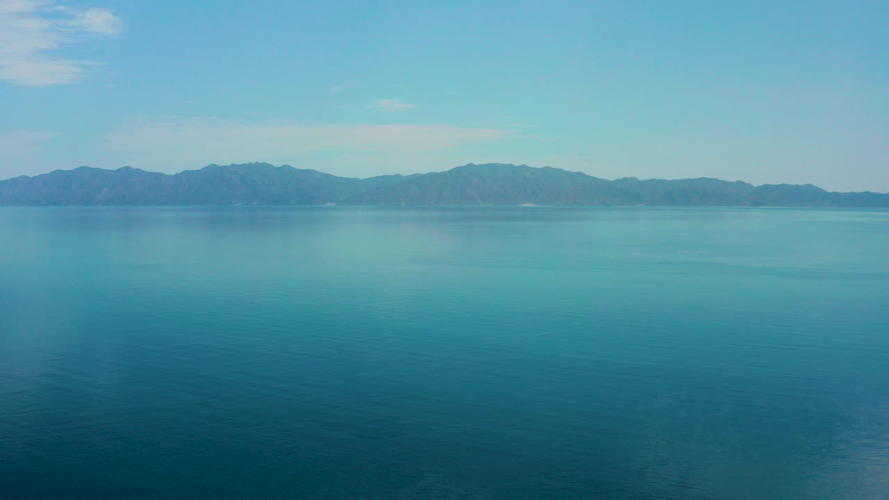 Opening frame of El Sargento La Ventana blue water stretching toward distant mountains under a pale sky, with no visible people.