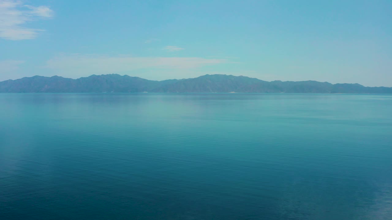 El Sargento La Ventana ocean appears aqua near the horizon and deeper blue in the foreground, with dark mountain silhouettes and no visible people.