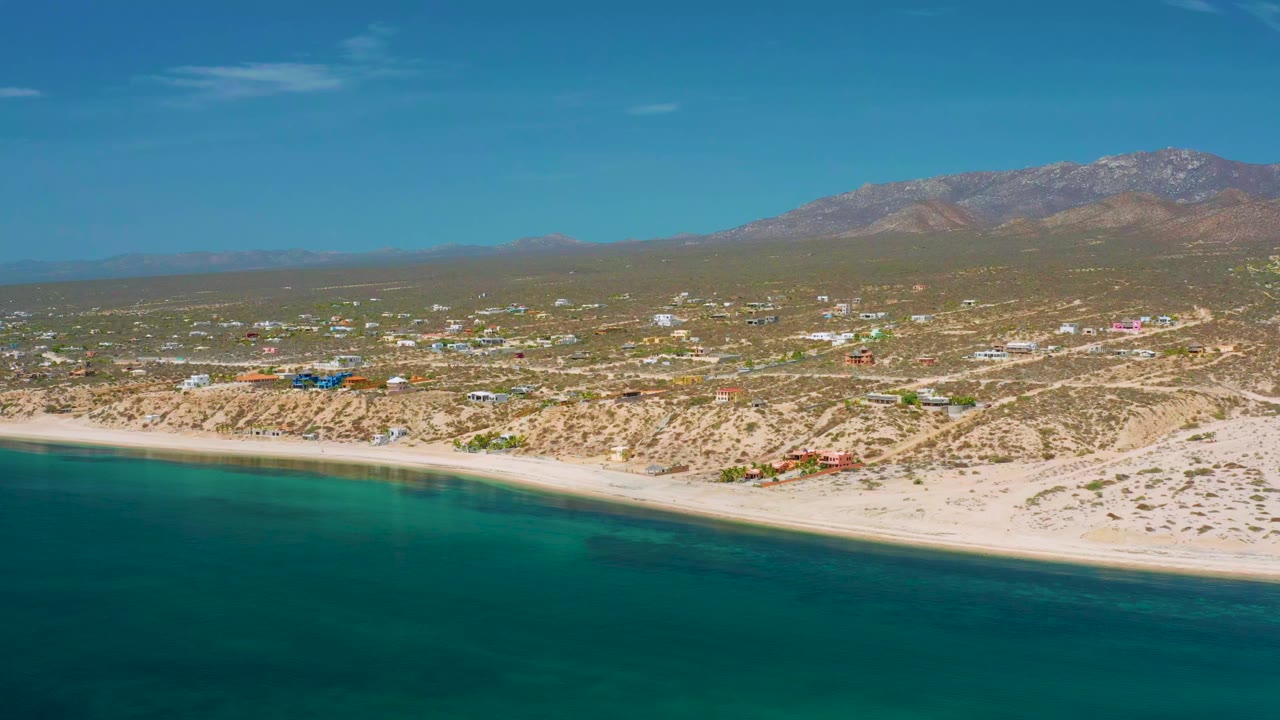 Aerial view of turquoise water, sandy beach, small town, and mountains.