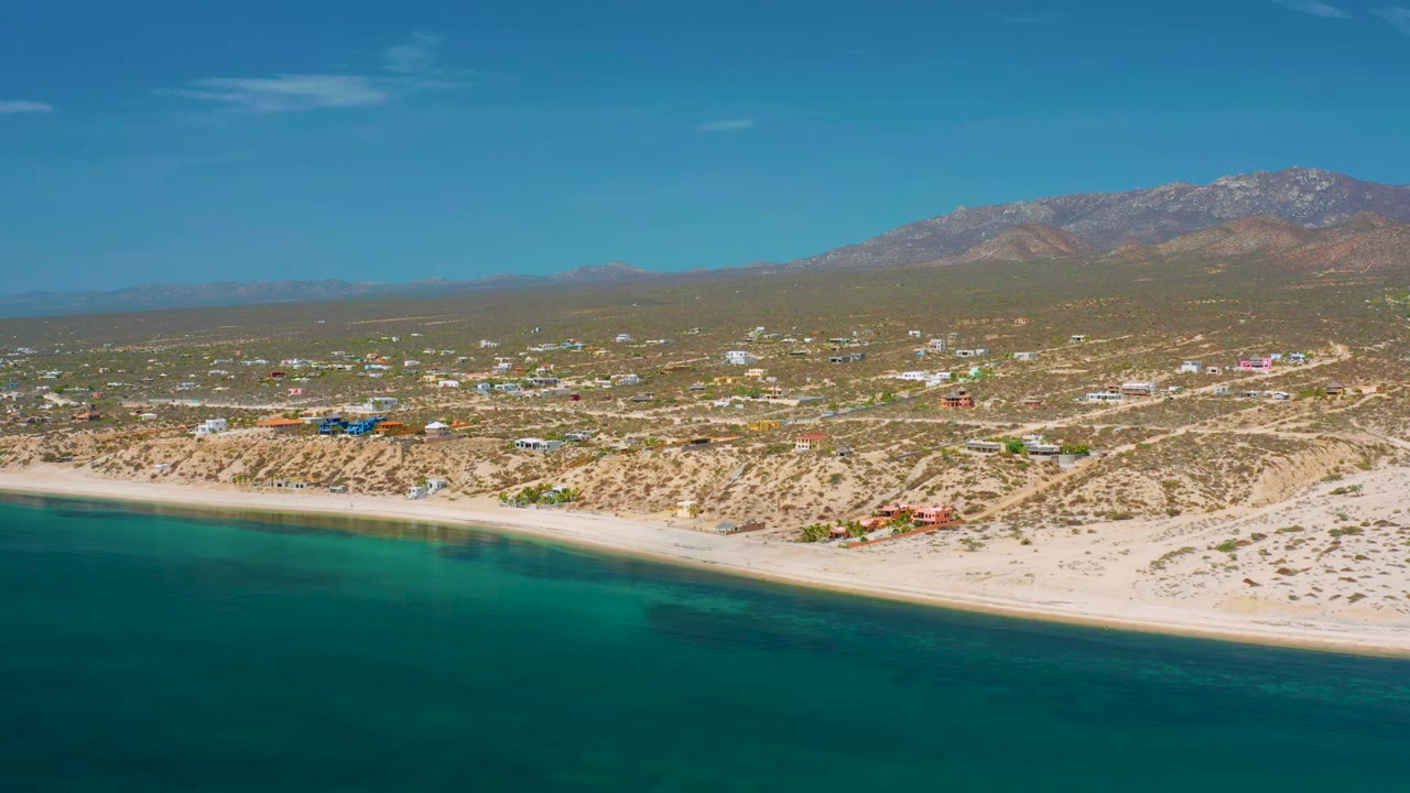 Aerial coastline with green-blue water, beach, town, and mountain ridge.