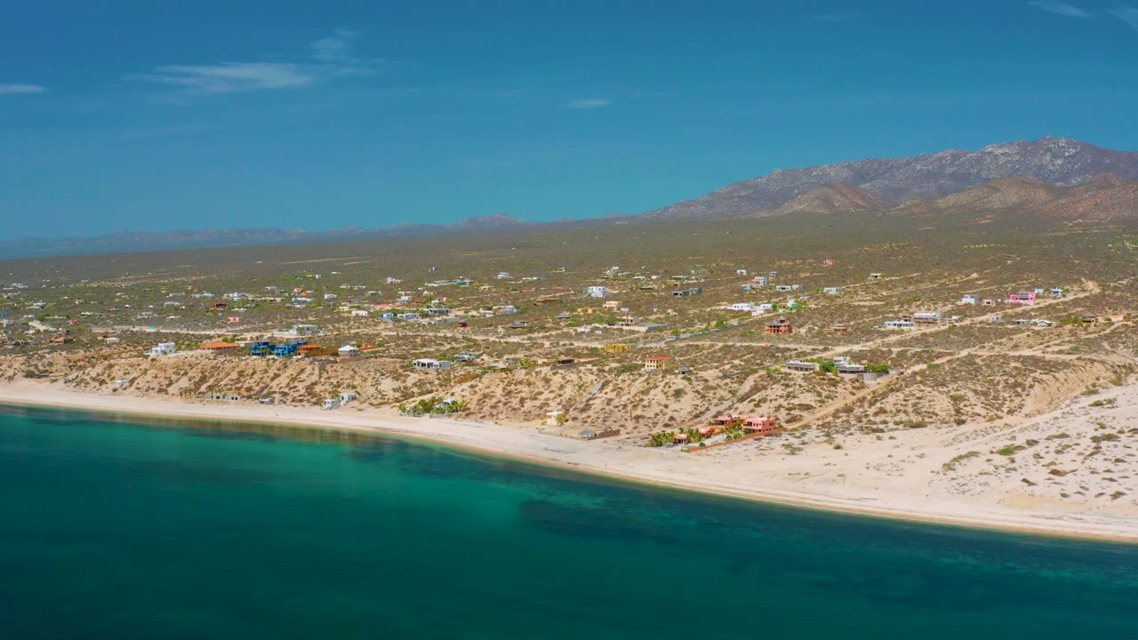 Aerial beach town view with turquoise water and dry mountain landscape.