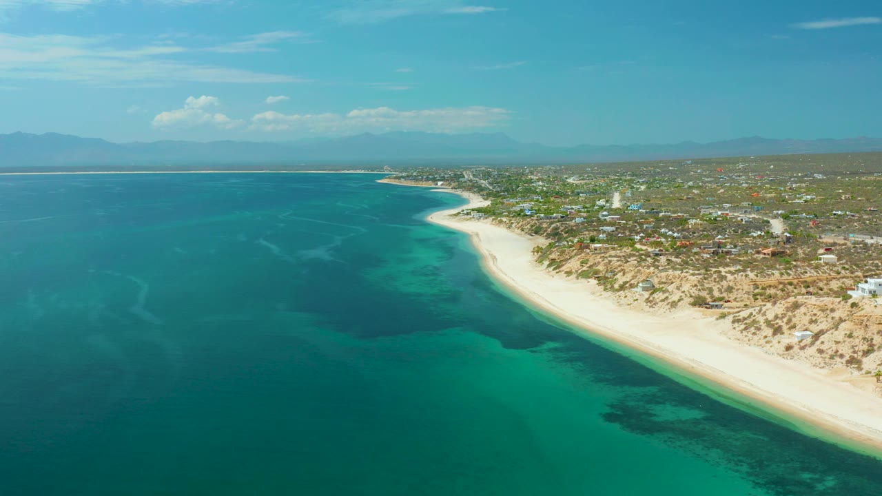 Blue sea beside a pale beach and low coastal settlement.