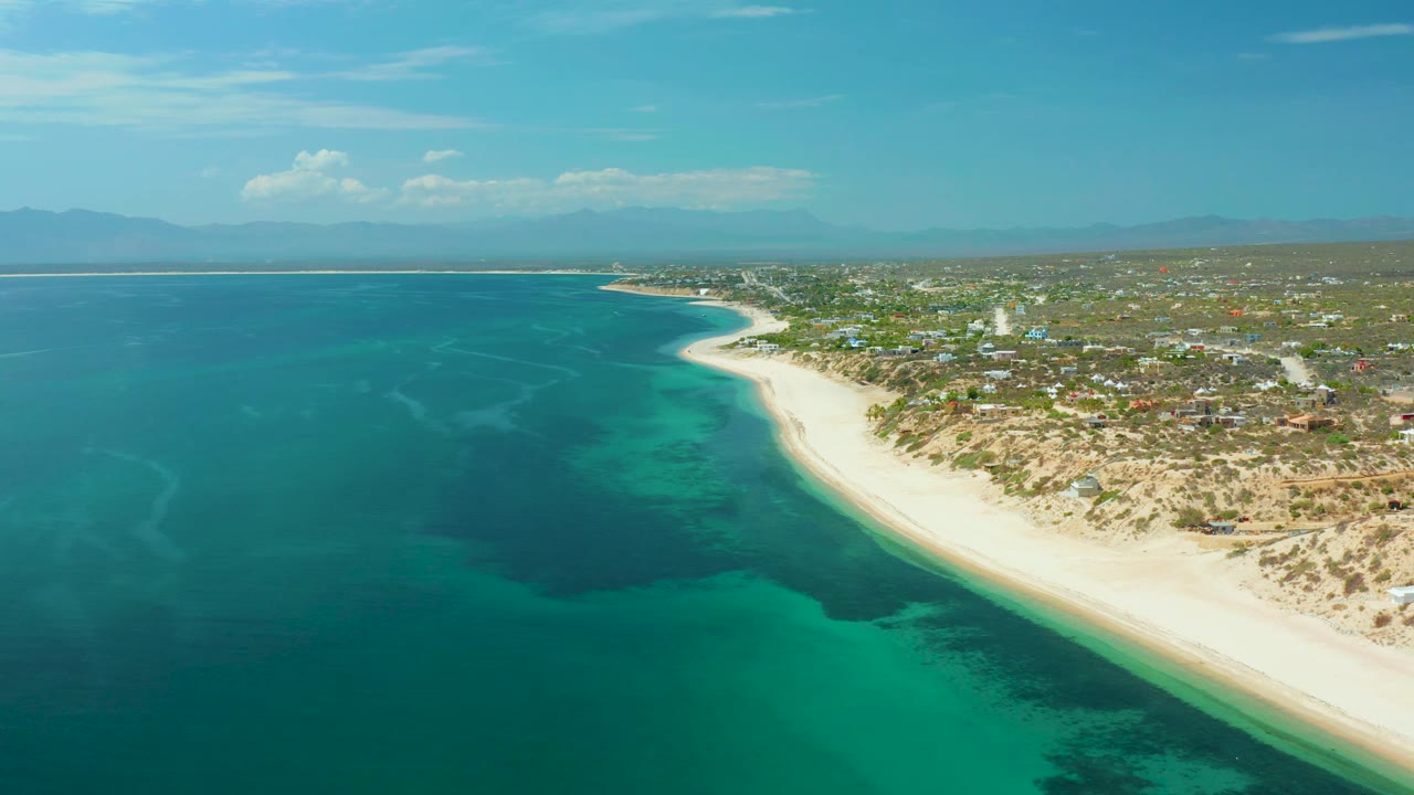 Wide aerial coastline with ocean on the left and beach settlement on the right.