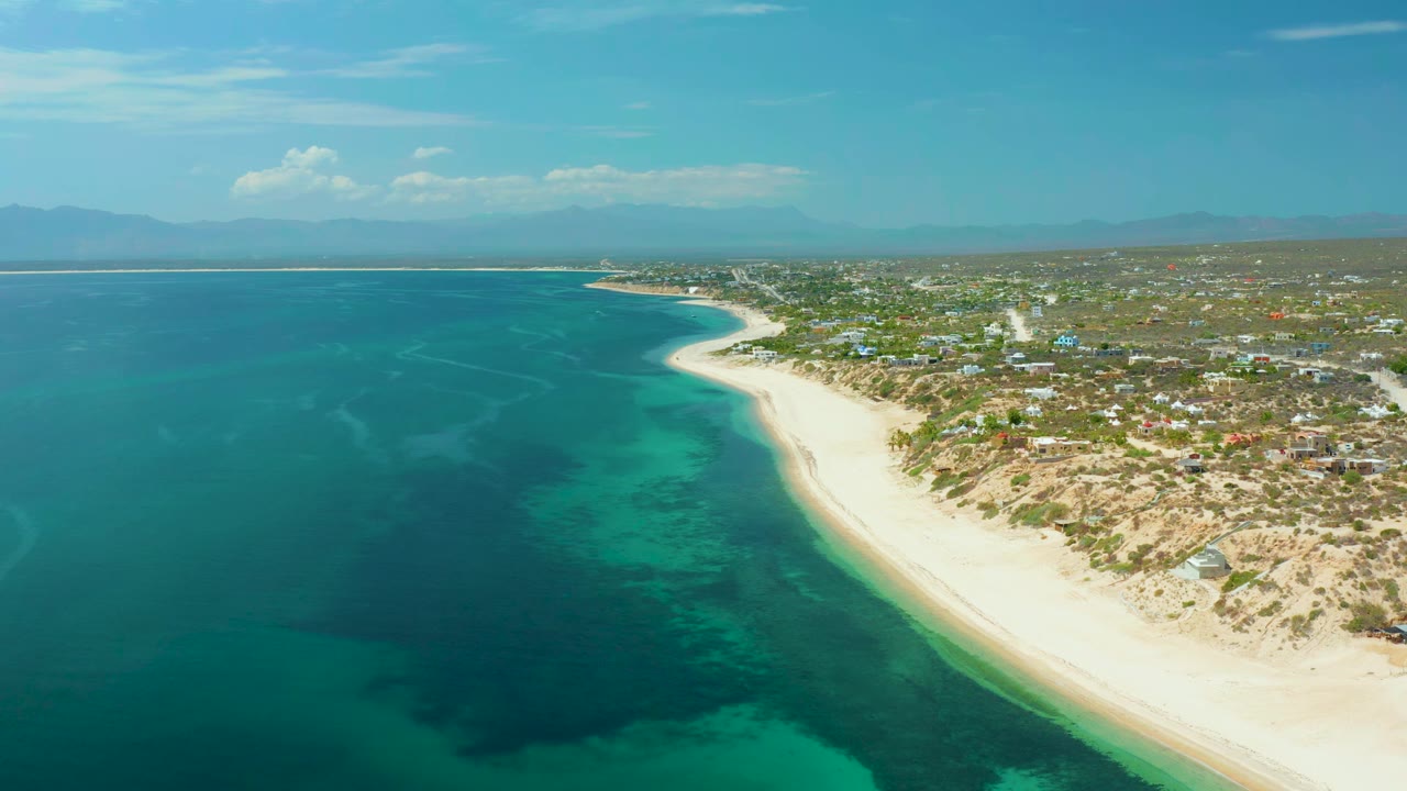 High aerial view of clear water beside a curving sandy beach and low town.