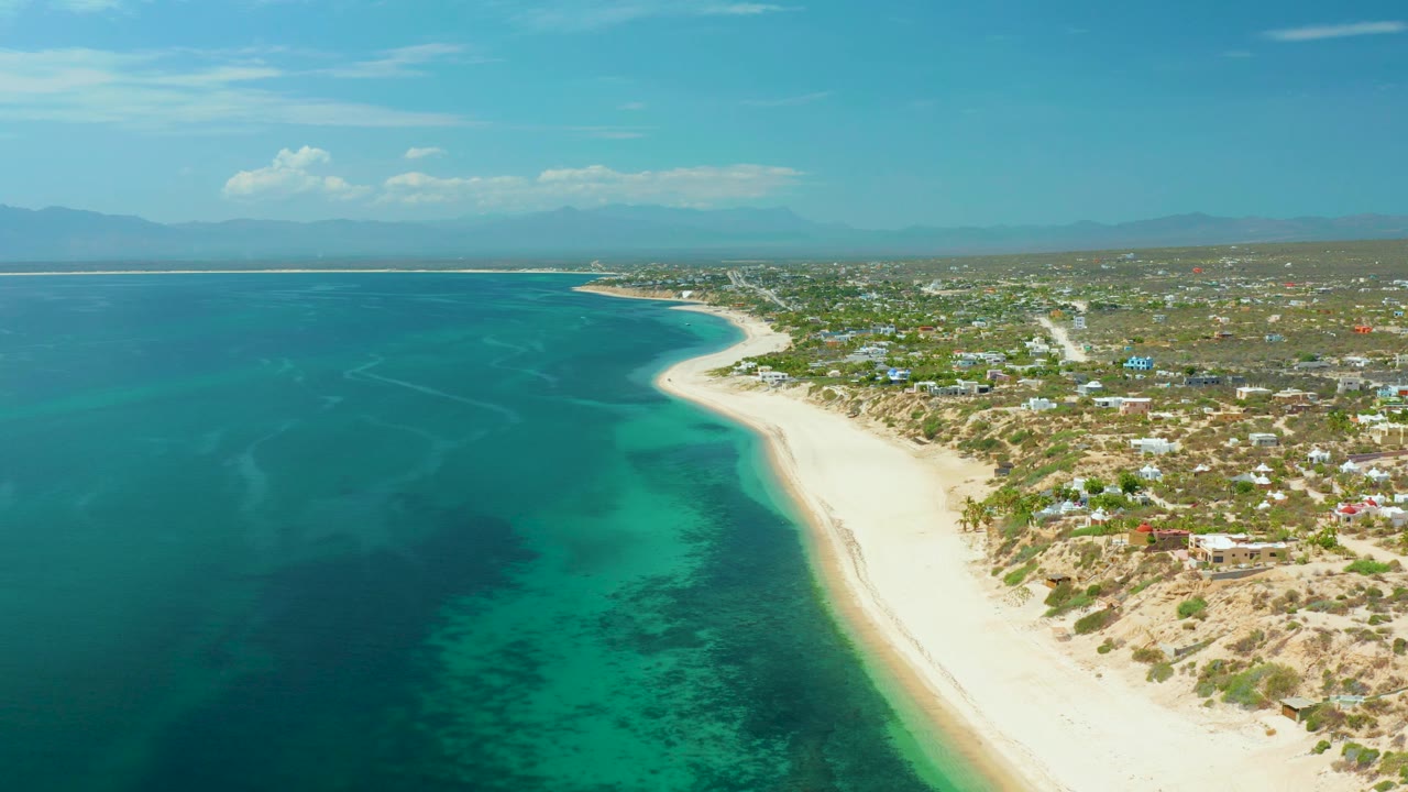 Bright aerial view of calm ocean beside a long sandy beach and inland roads.