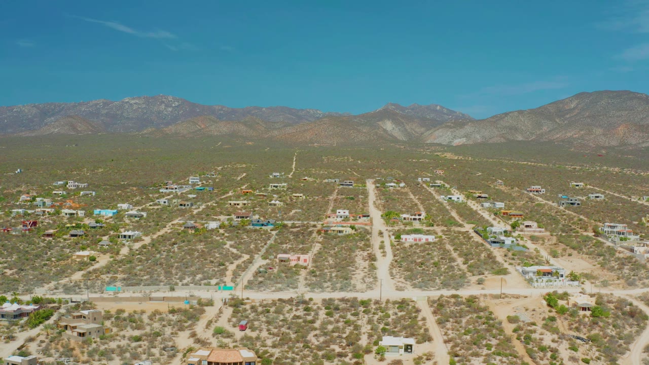 High view of a dry settlement with branching dirt roads and mountains beyond.
