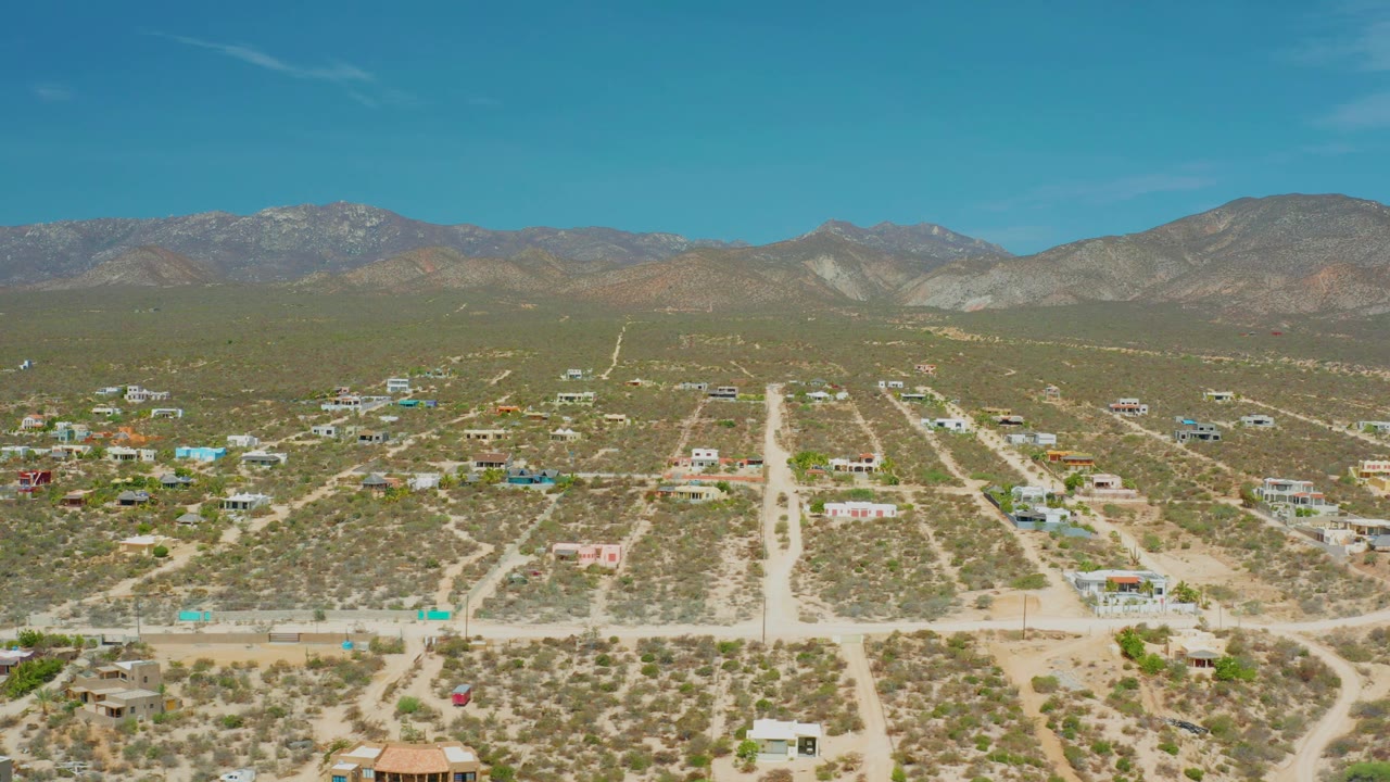 Aerial frame in El Sargento La Ventana, Mexico, showing more of the settlement spread across scrubby ground, light-colored roads, distant mountains, and no visible people.