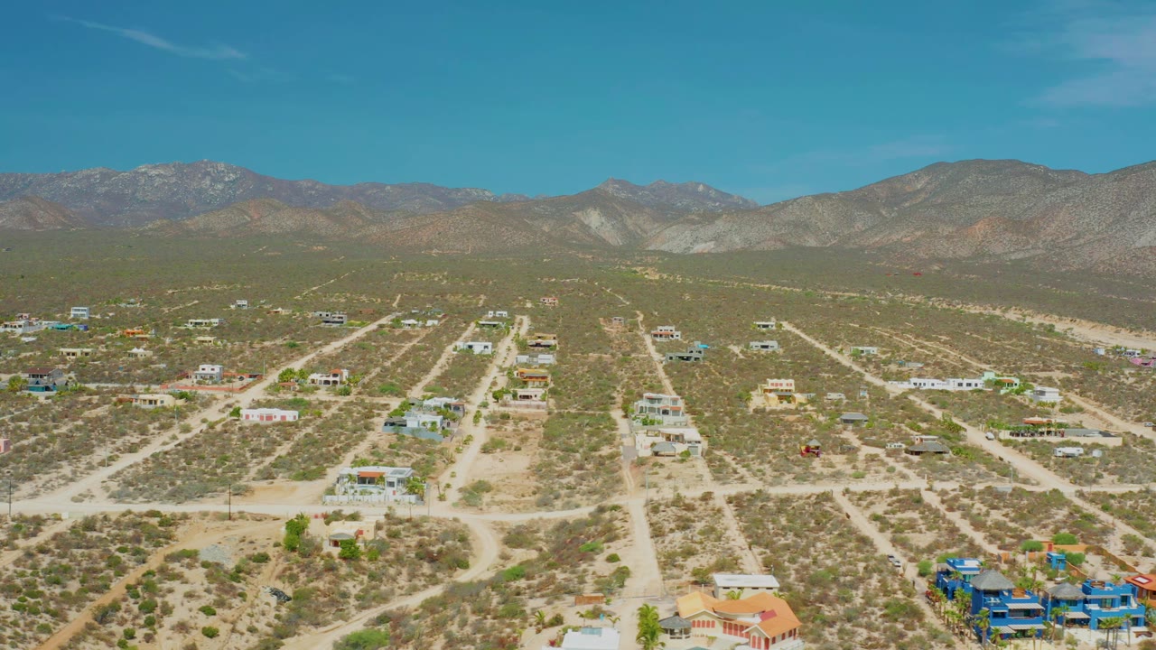 Drone view across dry village terrain toward a mountain ridge.