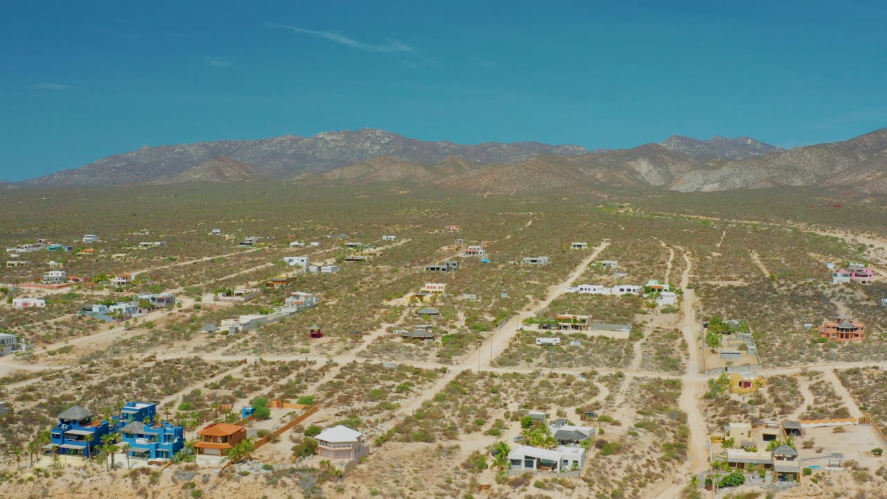 Opening aerial frame of El Sargento La Ventana, Mexico, with sandy roads, scattered low buildings, scrub desert, distant mountains, and no visible people.