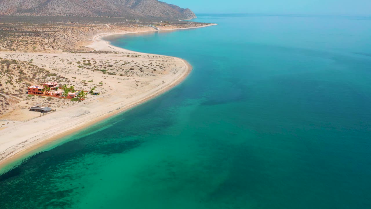 Curving sand spit and blue-green water seen from above.