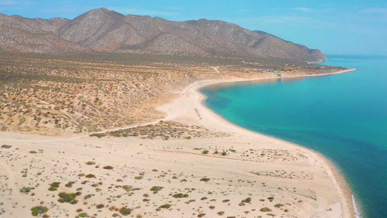 Aerial view of a desert shoreline, turquoise bay, and mountain ridge.
