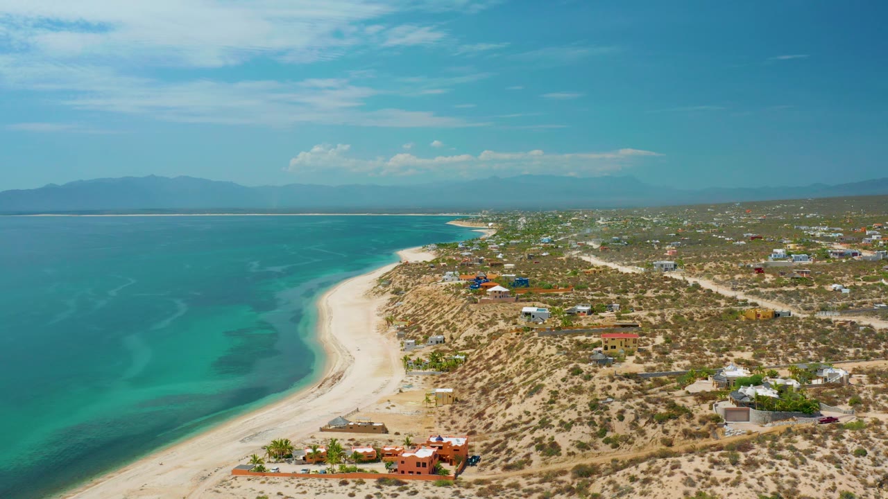 Wide drone frame of a quiet shoreline with aquamarine water and sparse coastal development.