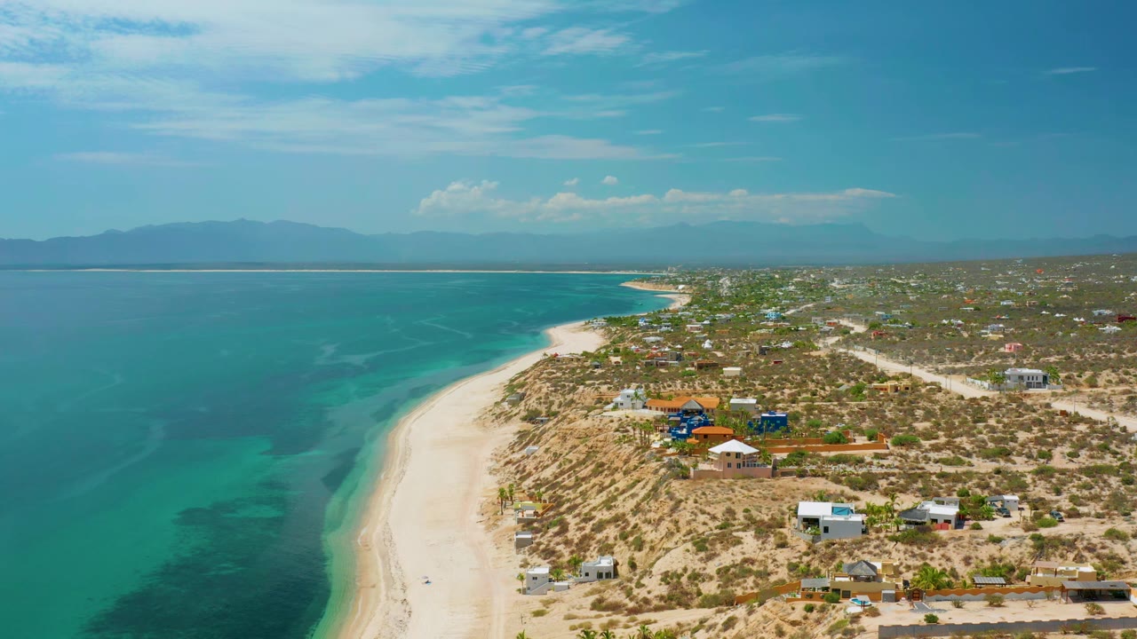 High coastal view with clear water beside a sandy beach and small buildings inland