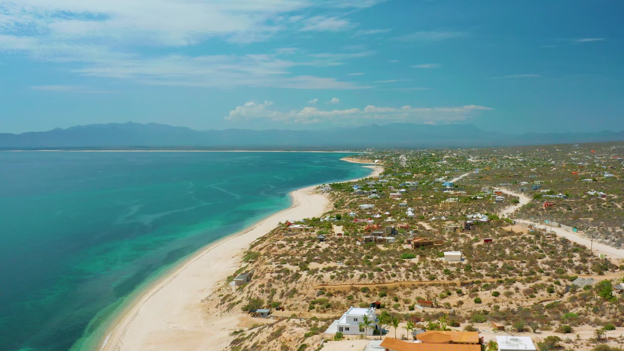 Wide aerial coastline with sea on the left and dry settlement land on the right.